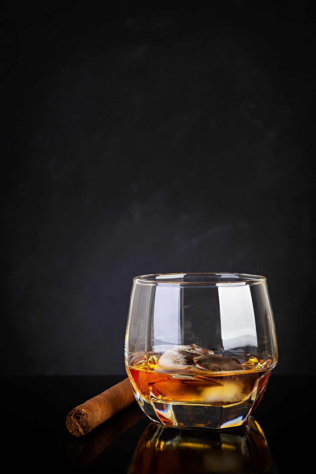 Glass of whiskey and cigar on dark background.